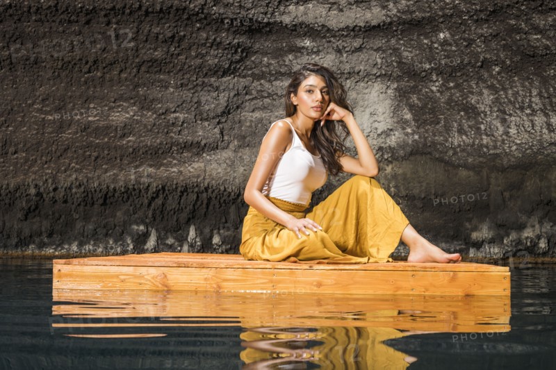 Beautiful woman sitting on wooden raft on pond