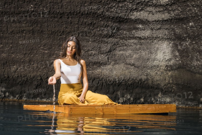 Beautiful woman sitting on wooden raft on pond