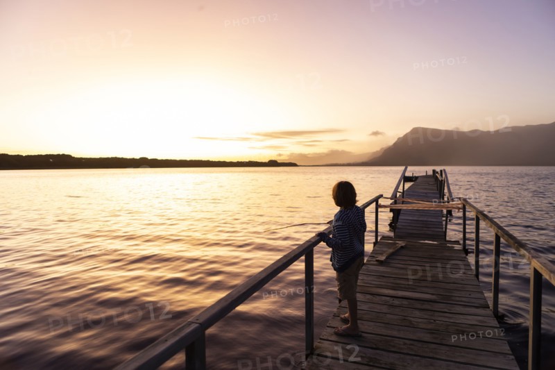 Boy standing on pier at lagoon at sunset