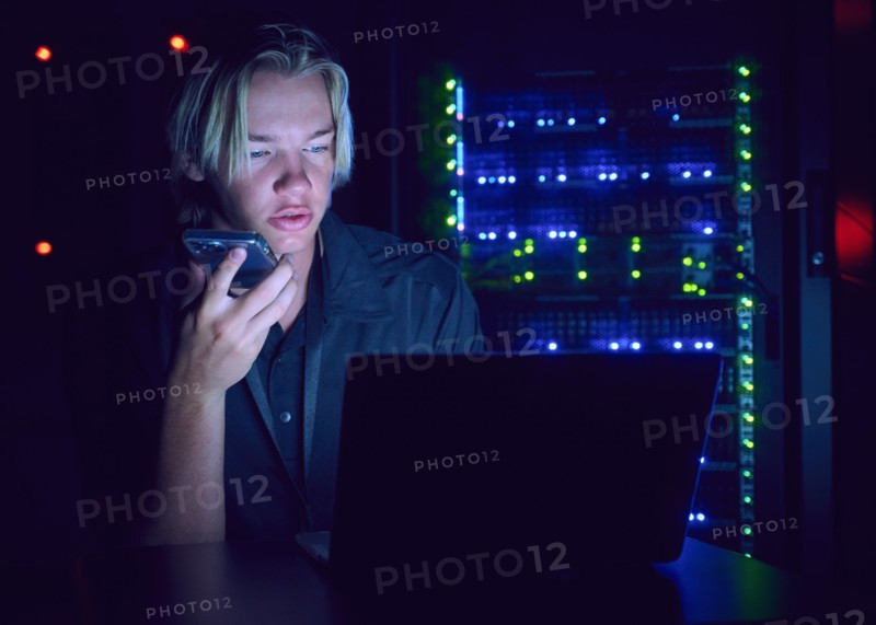 Technician using laptop and smart phone in server room