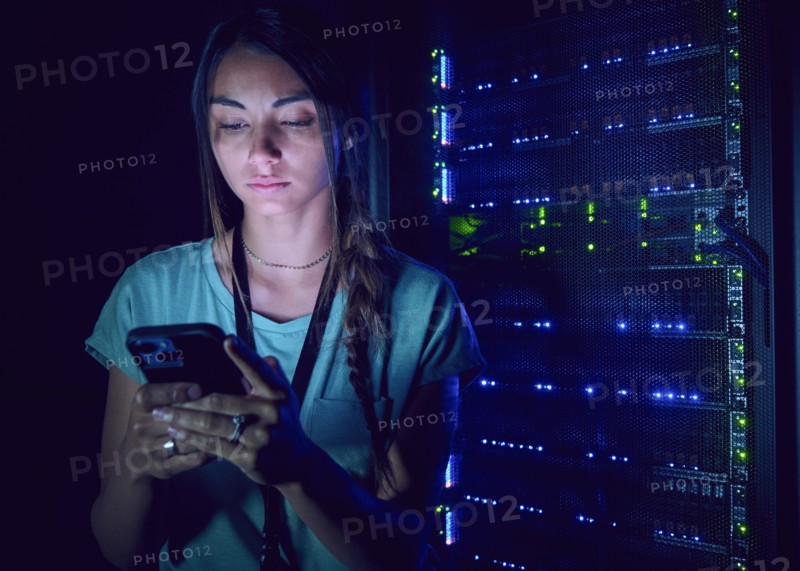 Female technician using smart phone in server room