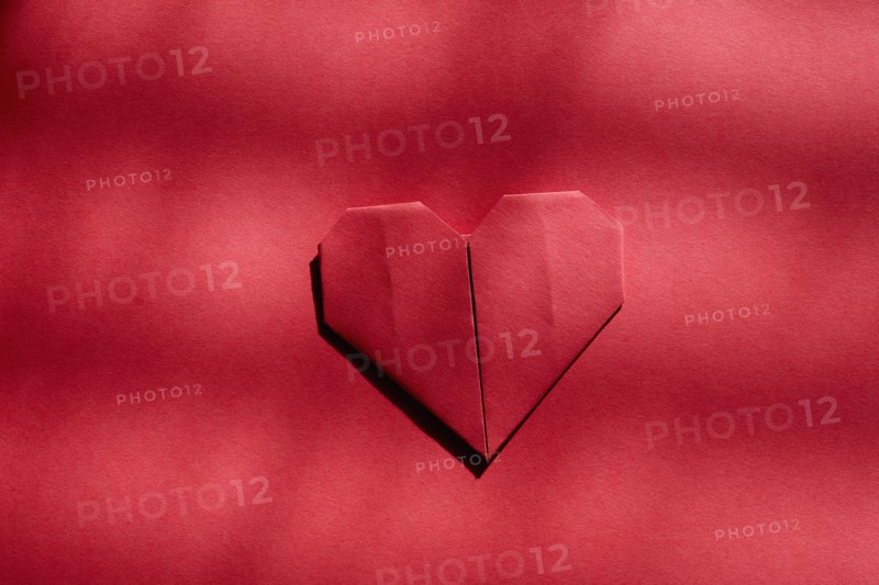 Red origami heart on red background