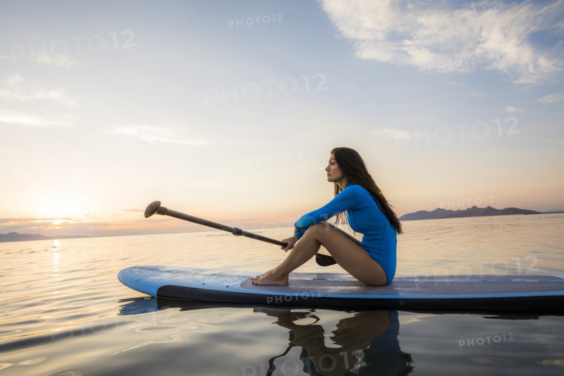 Woman sitting on paddleboard at sunset