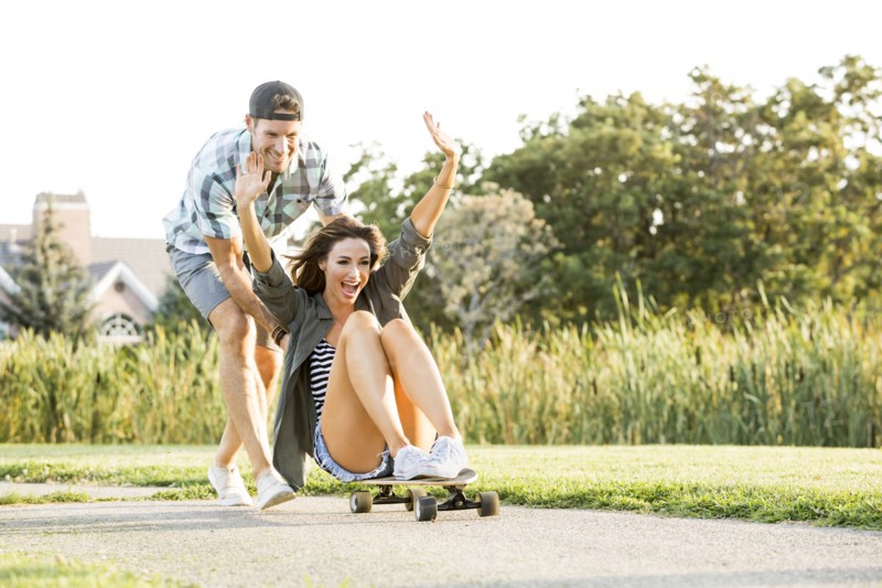 Man pushing woman sitting on longboard in park