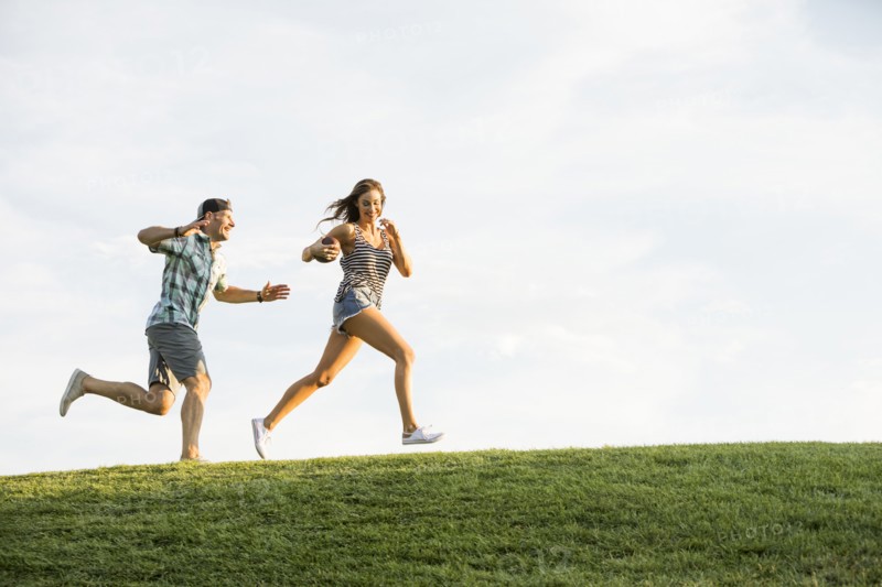 Woman and man running on grassy hill in park