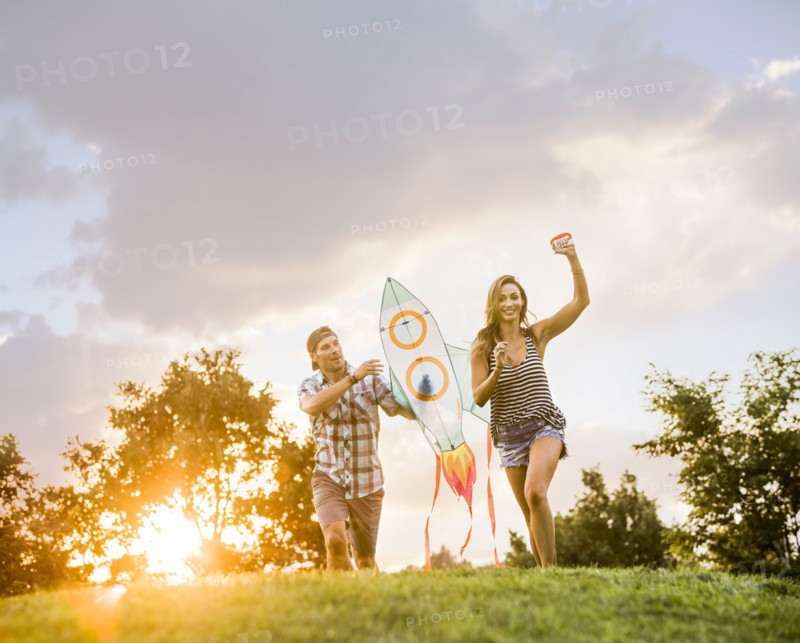 Woman and man running with kite in park at sunset