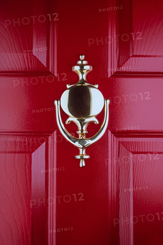 Close-up of old fashioned brass door knocker on red front door