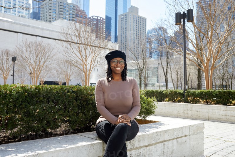 Portrait of smiling woman wearing eyeglasses and beret sitting on wall in city