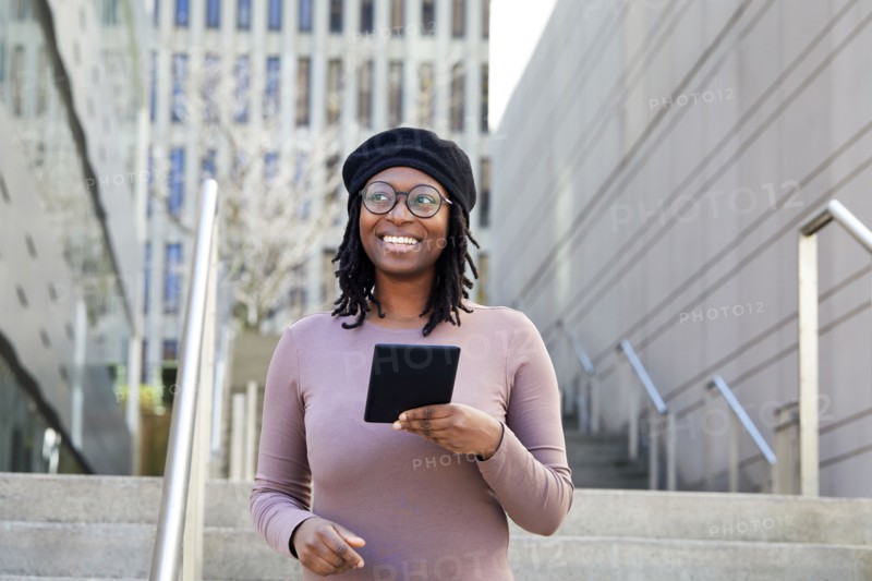 Smiling woman wearing eyeglasses and beret holding digital tablet in city