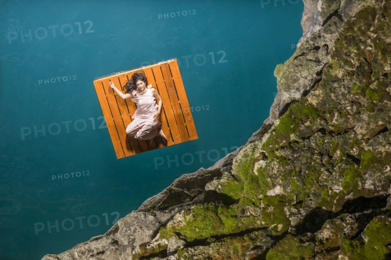 Overhead view of woman lying on floating dock near rocky coast
