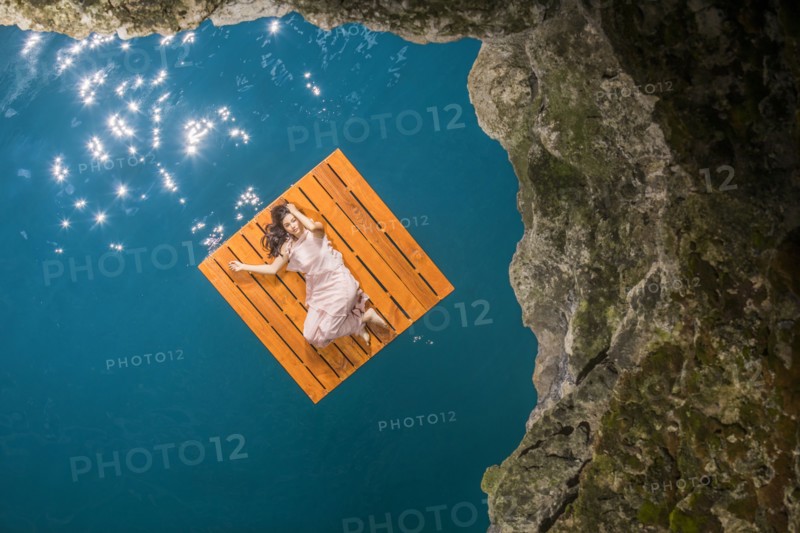 Overhead view of woman lying on floating dock near rocky coast