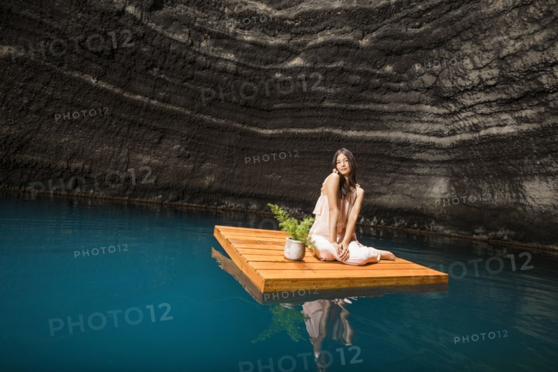 Portrait of woman sitting on floating dock near rocky coast