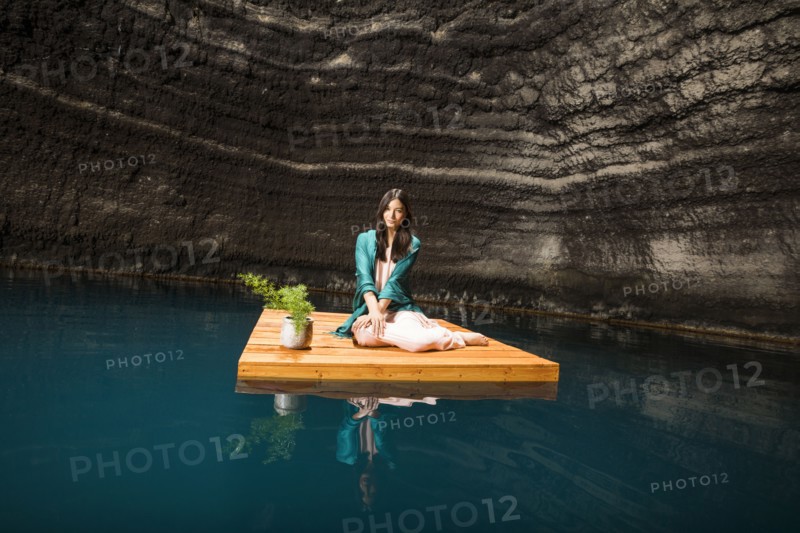 Portrait of woman sitting on floating dock near rocky coast
