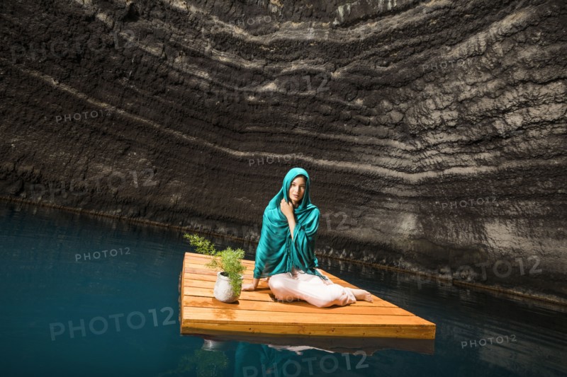 Portrait of woman sitting on floating dock near rocky coast