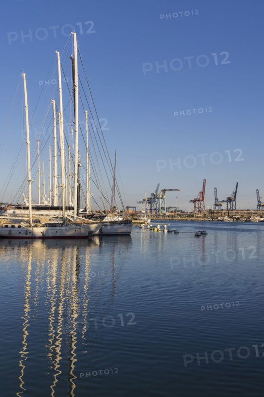 Sailboats moored at marina with dock cranes in background