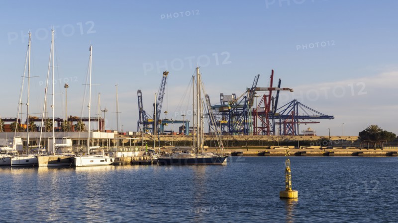 Sailboats moored at marina with dock cranes in background