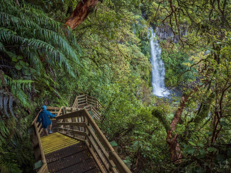 Hiker walking down wooden stairs towards waterfall