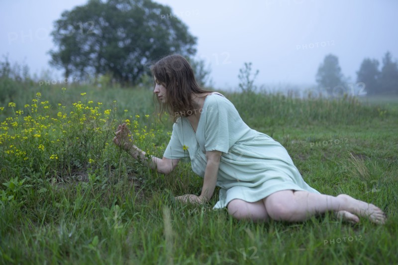 Woman looking at flowers in meadow on foggy day