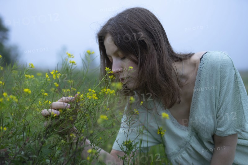 Woman smelling flowers in meadow on foggy day