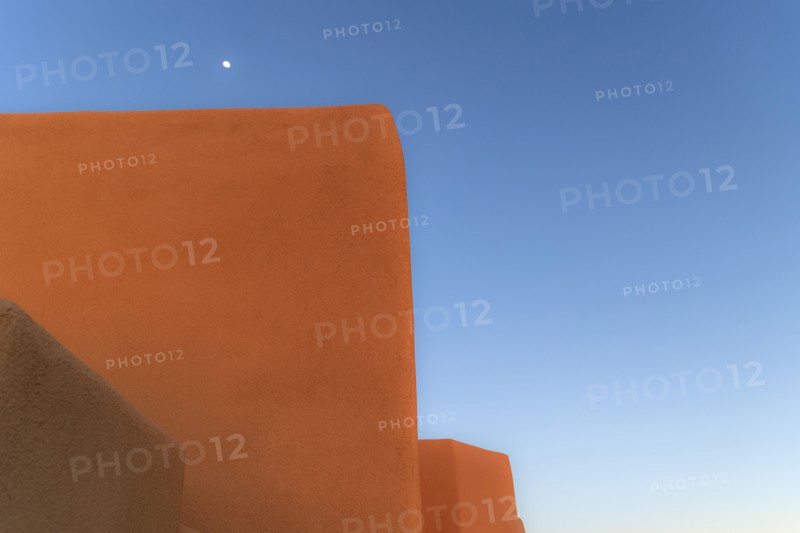 Moon in blue sky above adobe walls