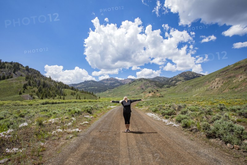 Senior woman standing with arms outstretched on road in mountain scenery