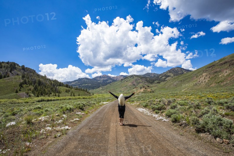 Rear view of senior woman standing with arms raised on road and looking at mountains