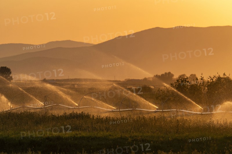 Farm irrigation system with mountain landscape in background at sunset