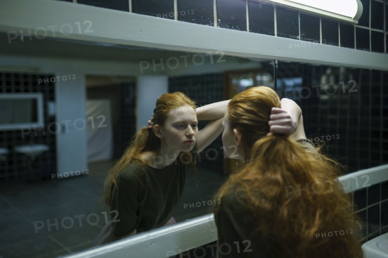 Young woman looking in mirror in public bathroom
