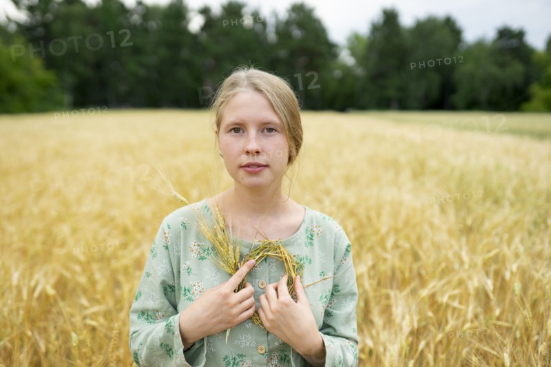 Portrait of young woman holding small wreath in wheat field