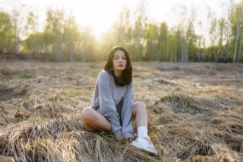 Brunette woman wearing grey sweatshirt sitting in meadow