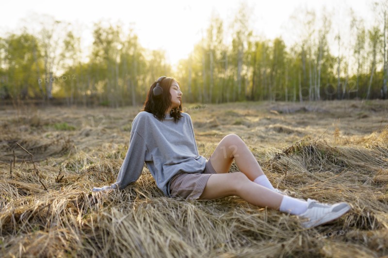 Brunette woman sitting in meadow and listening to music