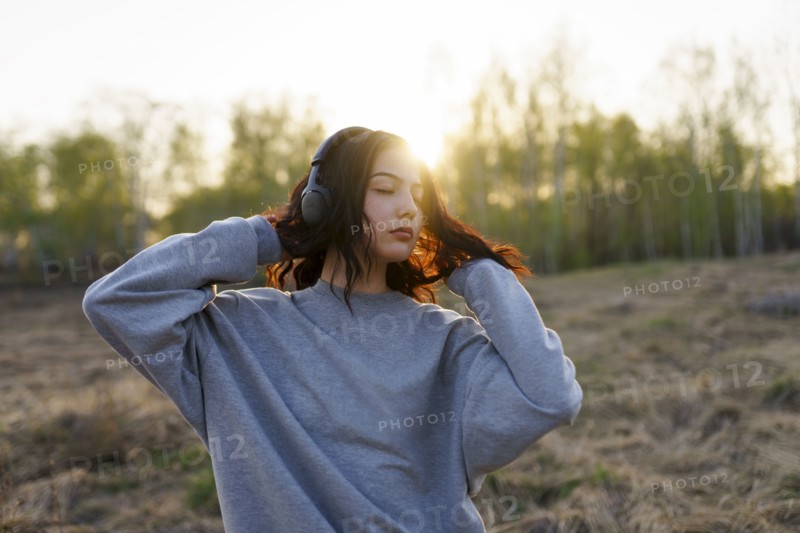 Portrait of woman listening to music with closed eyes in meadow at sunset