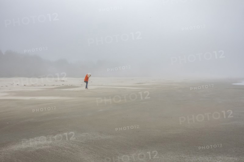Woman in orange jacket standing on foggy beach