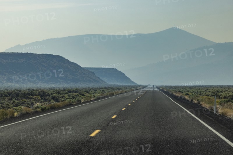 Empty highway leading through desert with mountains in background