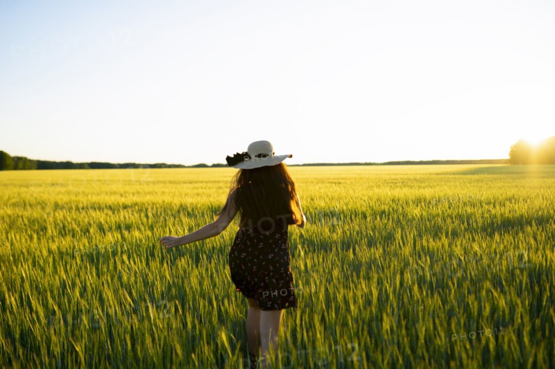 Rear view of woman in straw hat walking in field at sunset
