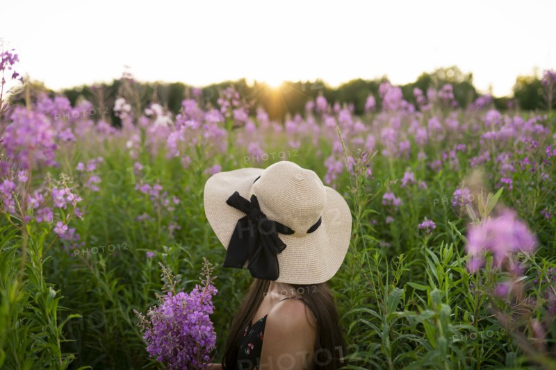 Side view of young woman looking at flowers on meadow