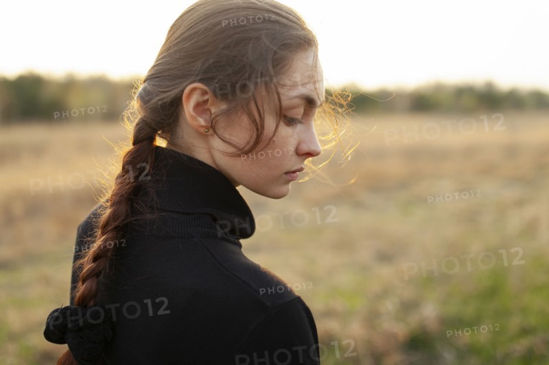 Side view of serious woman standing in field at sunset