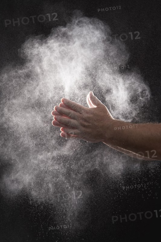 Baker dusting flour off his hands against black background