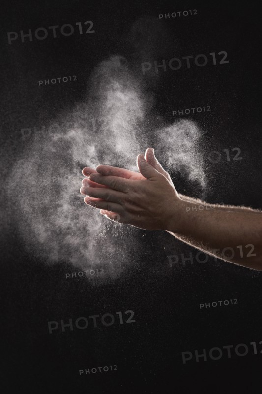 Baker dusting flour off his hands against black background