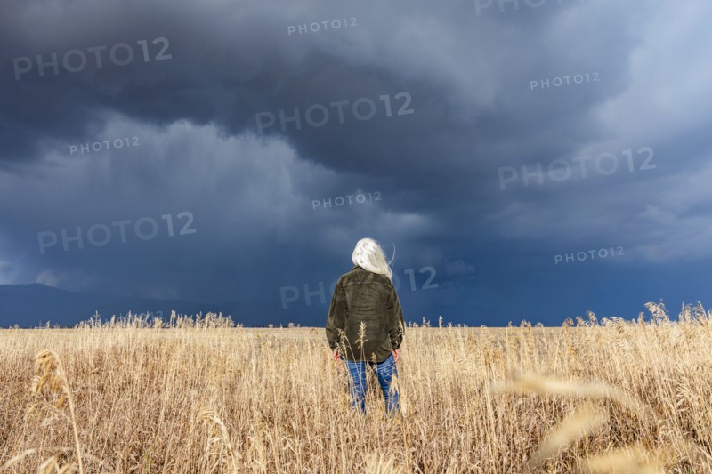 Rear view of woman standing in fall grasses under stormy sky, Fairfield, Idaho, USA