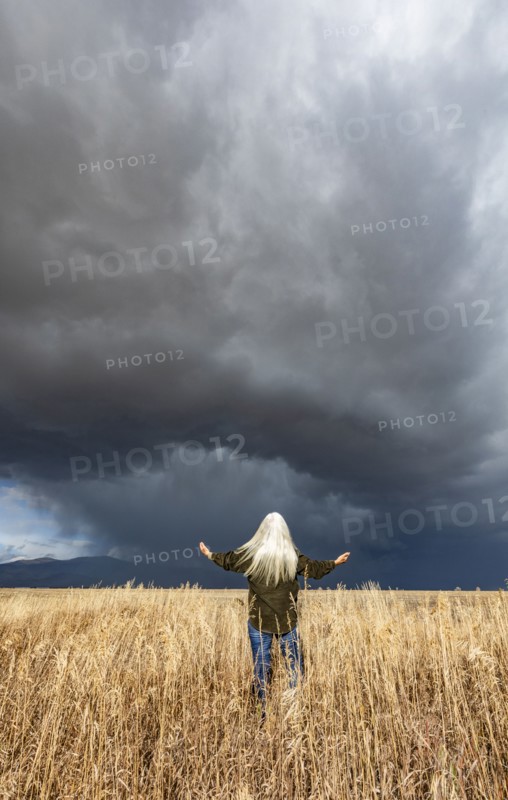 Rear view of woman standing in fall grasses under stormy sky, Fairfield, Idaho, USA