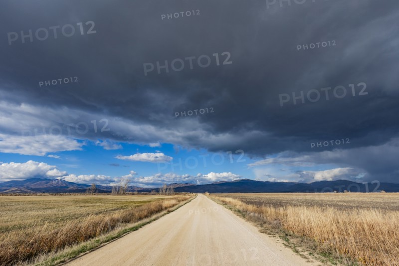 Dark storm clouds over dirt road crossing field, Fairfield, Idaho, USA