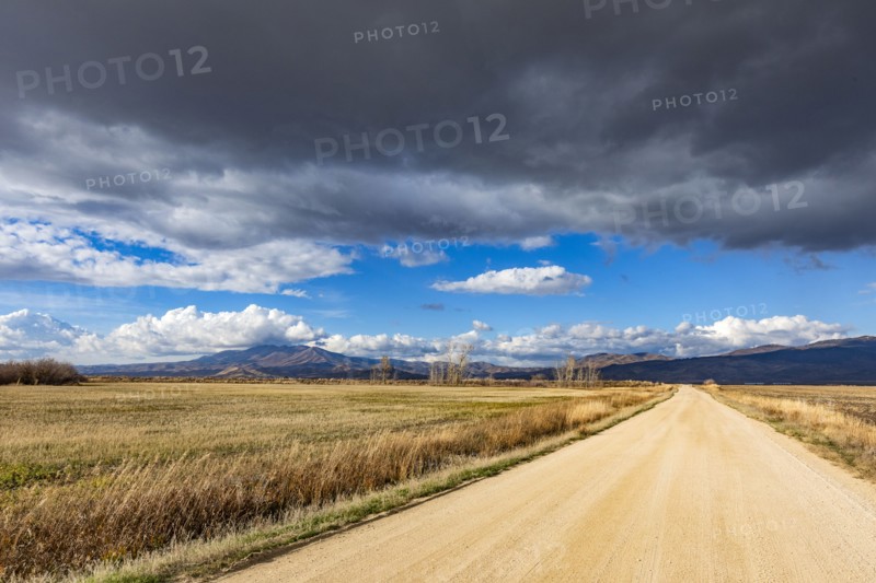 Dark storm clouds over dirt road crossing field, Fairfield, Idaho, USA