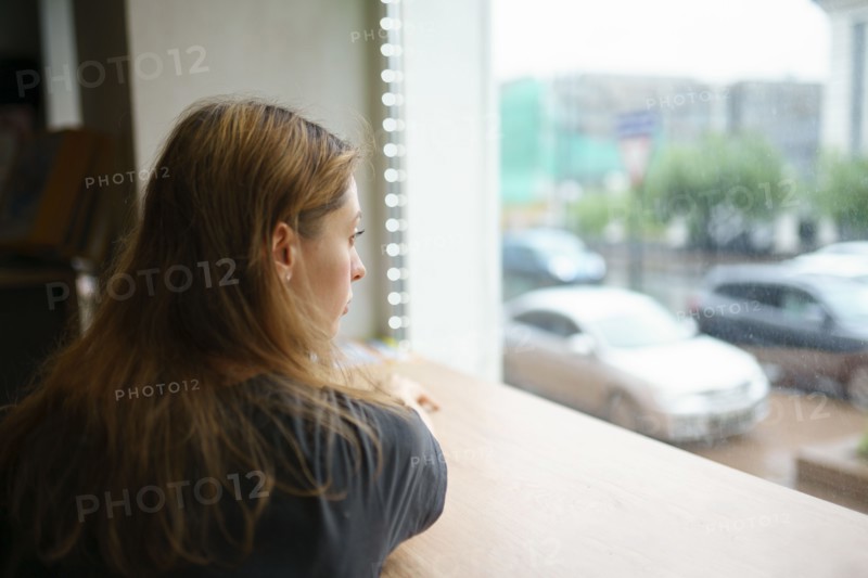 Woman leaning on window sill and looking through window, Omsk, , Russia