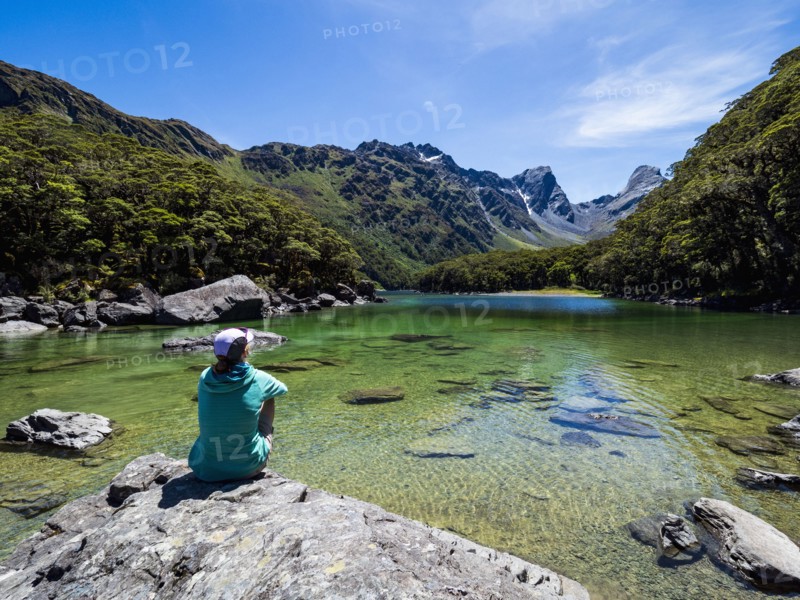 Rear view of woman sitting on lakeshore in Fiordland National Park, Te Anau, Fiordland, New Zealand