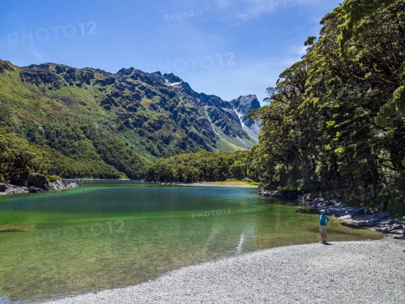 Rear view of woman sitting on lakeshore in Fiordland National Park, Te Anau, Fiordland, New Zealand