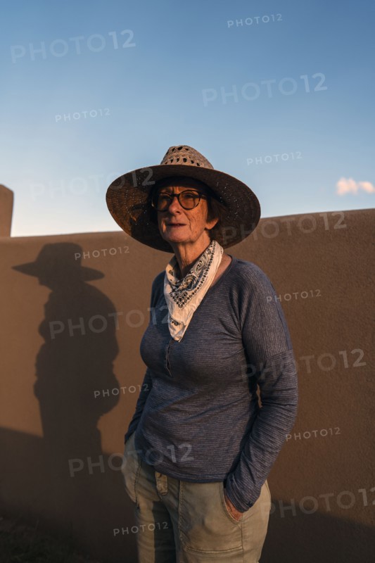 Usa, New Mexico, Santa Fe, Portrait of woman in straw hat standing against adobe wall in High Desert, Santa Fe, New Mexico, USA