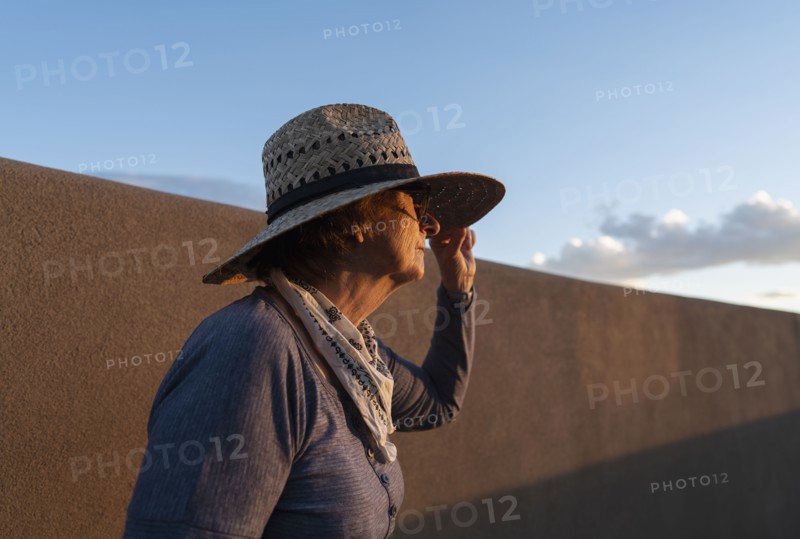 Usa, New Mexico, Santa Fe, Woman in straw hat standing against adobe wall in High Desert, Santa Fe, New Mexico, USA