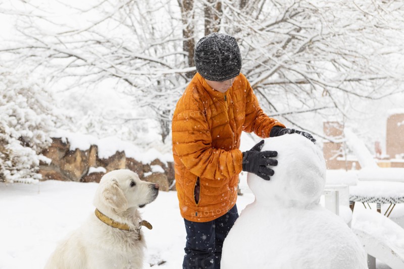 Boy with his dog building snowman, Santa Fe, New Mexico, USA