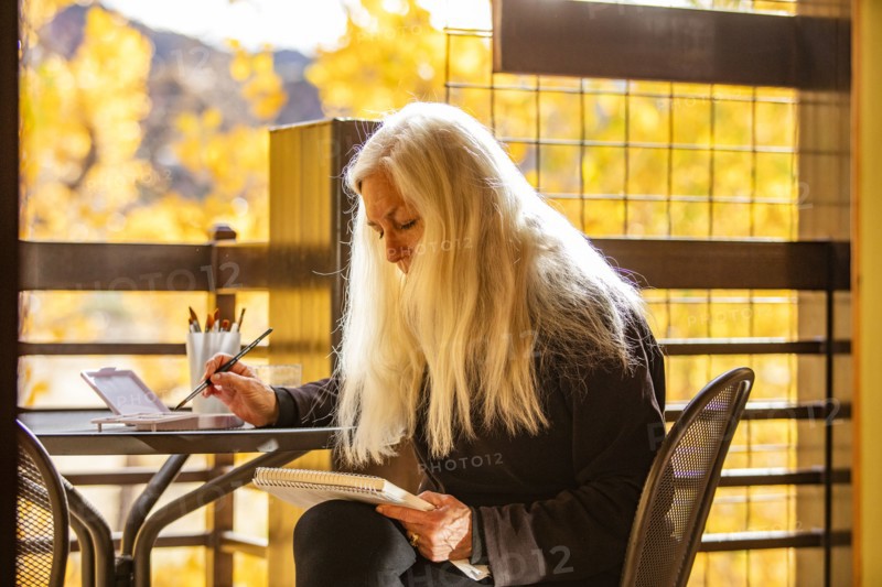 Woman with long white hair painting watercolors on deck in autumn, Springdale, Utah, USA